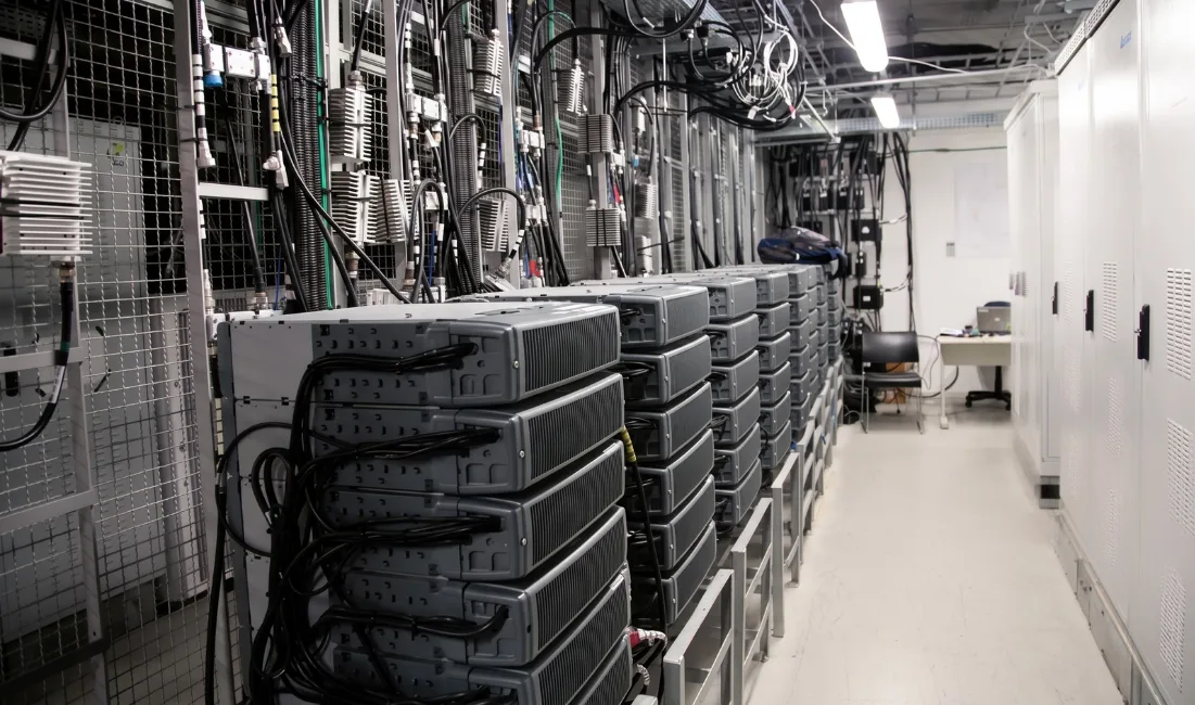 An indoor view of a telecom data center and server room featuring rows of network switches, heavy-duty cabling infrastructure, and equipment cabinets.